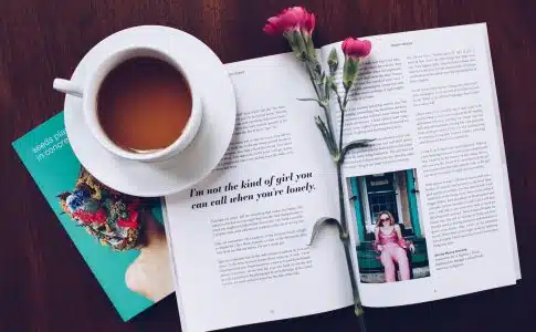 opened book with pink flower on top near filled ceramic mug